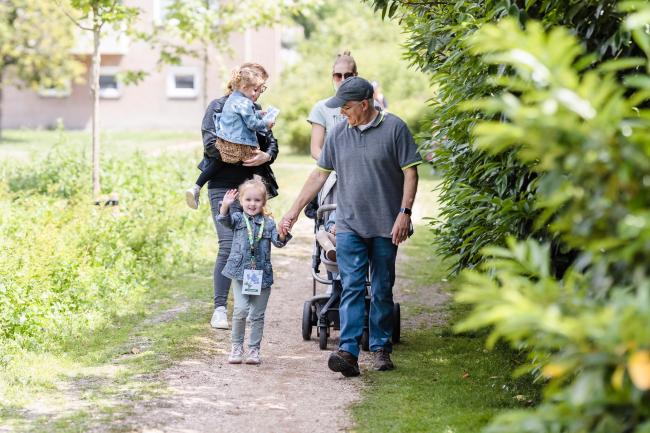 Meisje dat zwaait naar de camera hand in hand met haar opa wandelend in een groene omgeving