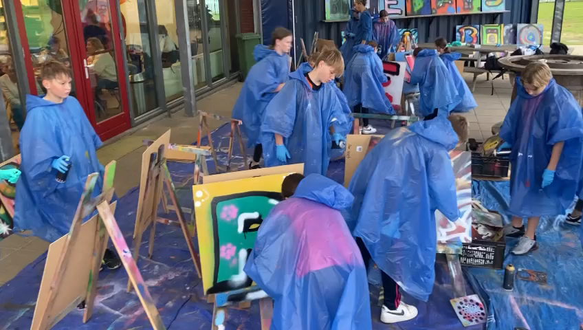 Kinderen die bezig zijn met een workshop graffiti en op schilderdoeken met graffiti spuiten.