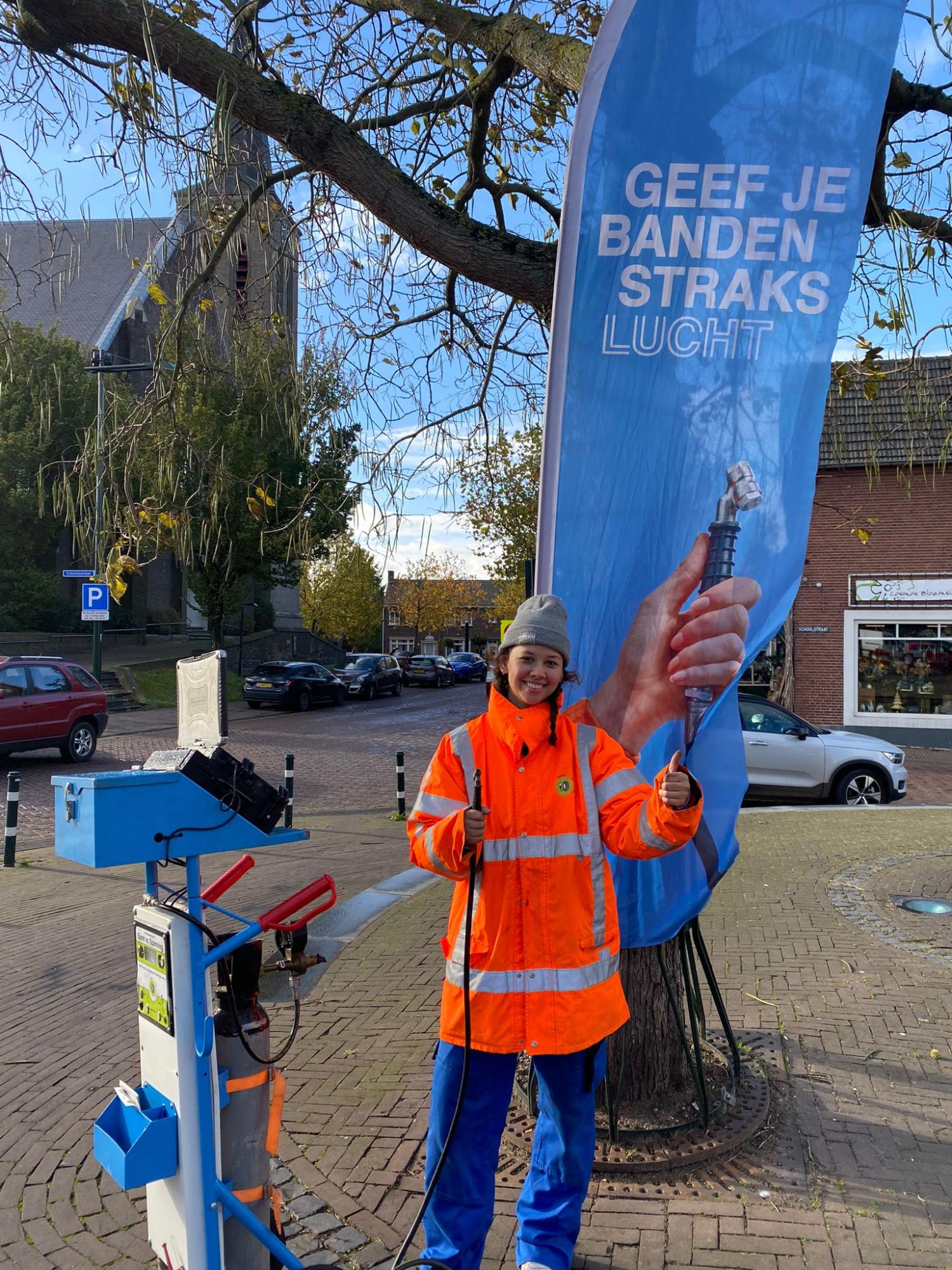Vrouw in oranje jas met apparaat om bandenspanning te controleren