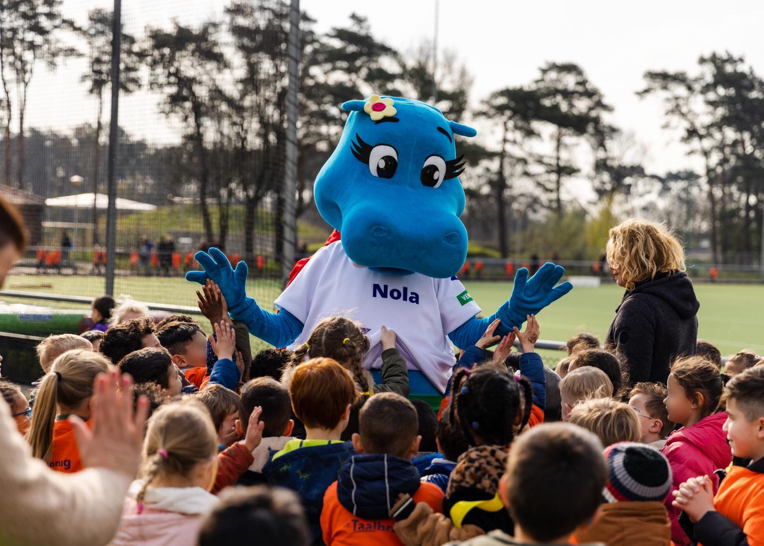 Nijlpaard mascotte met groep kinderen ervoor bij een sportveld