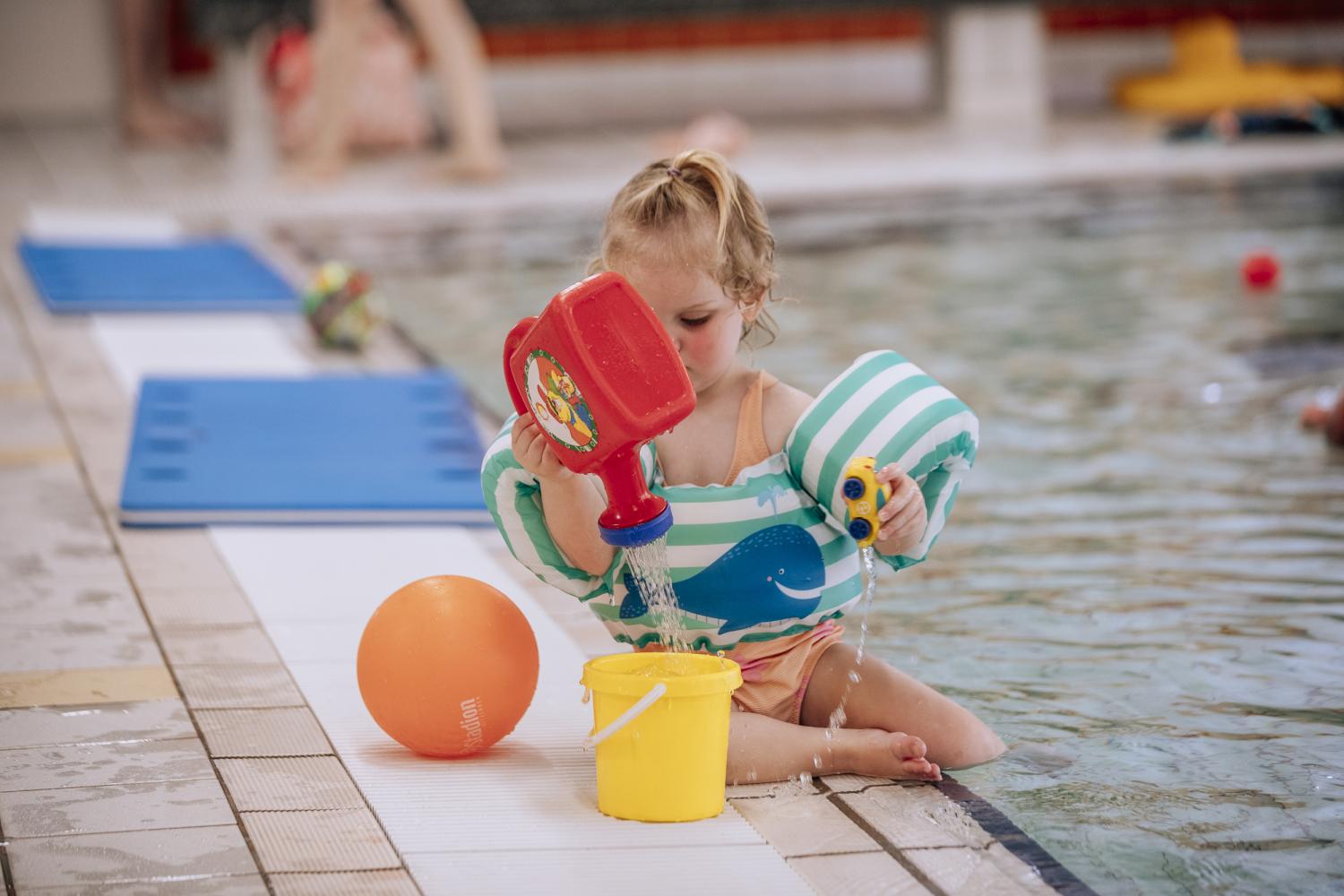 Kleuter aan het spelen bij het zwembad met een emmer, gieter en een balletje